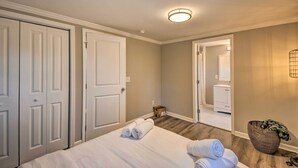 A hotel room with a bed, two doors, a small table with towels, a basket, and a mirror in the corner. - Private Yard + Fire Pit: Commerce Home! (Commerce)