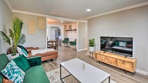 A modern living room with a sofa, coffee table, TV, and a dining area in the background. - Private Yard + Fire Pit: Commerce Home! (Commerce)