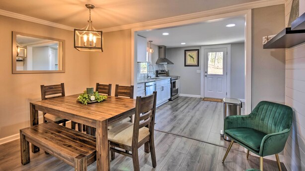 A dining area with a wooden table and chairs, a green upholstered chair, and a kitchen in the background. - Private Yard + Fire Pit: Commerce Home! (Commerce)