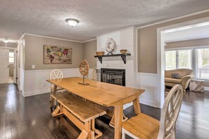 A spacious living room with a wooden dining table and benches, a fireplace, and a large window.