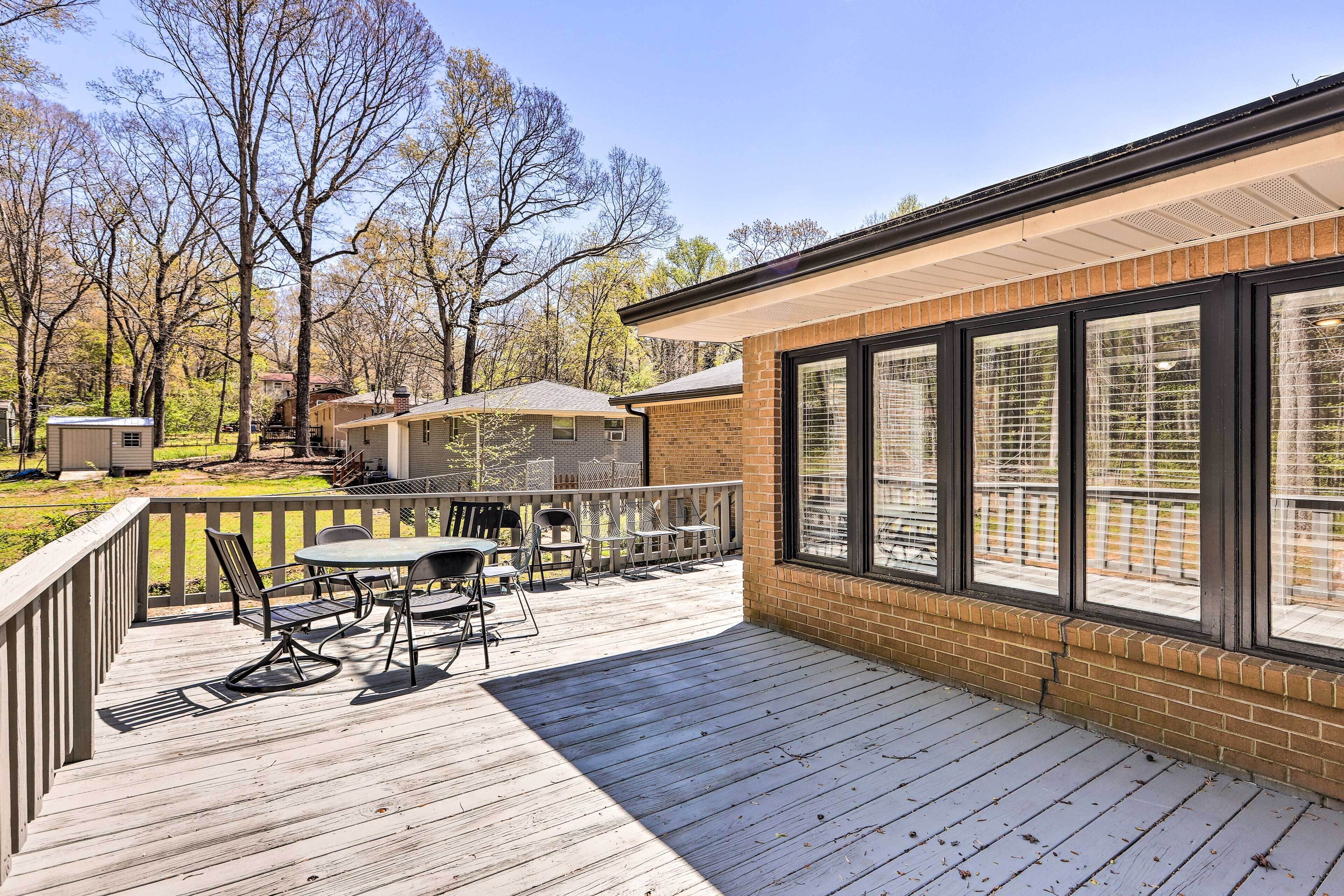 A wooden deck with outdoor furniture, a brick building with large windows, and a fenced yard.