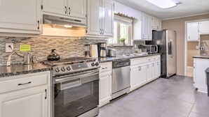 Una cocina moderna con armarios blancos, electrodomésticos de acero inoxidable, un salpicadero de azulejos y un ventanal con vistas a árboles.