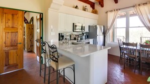 A spacious kitchen with white cabinets, a central island with bar stools, and a dining area with wooden chairs. - Mountain Views & Private Jacuzzi: Tucson Casita (Tucson)