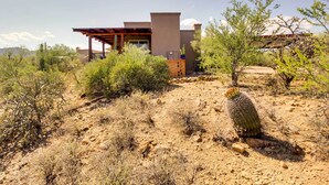 A modern house with a flat roof, a covered patio, and a desert landscape with sparse vegetation. - Mountain Views & Private Jacuzzi: Tucson Casita (Tucson)