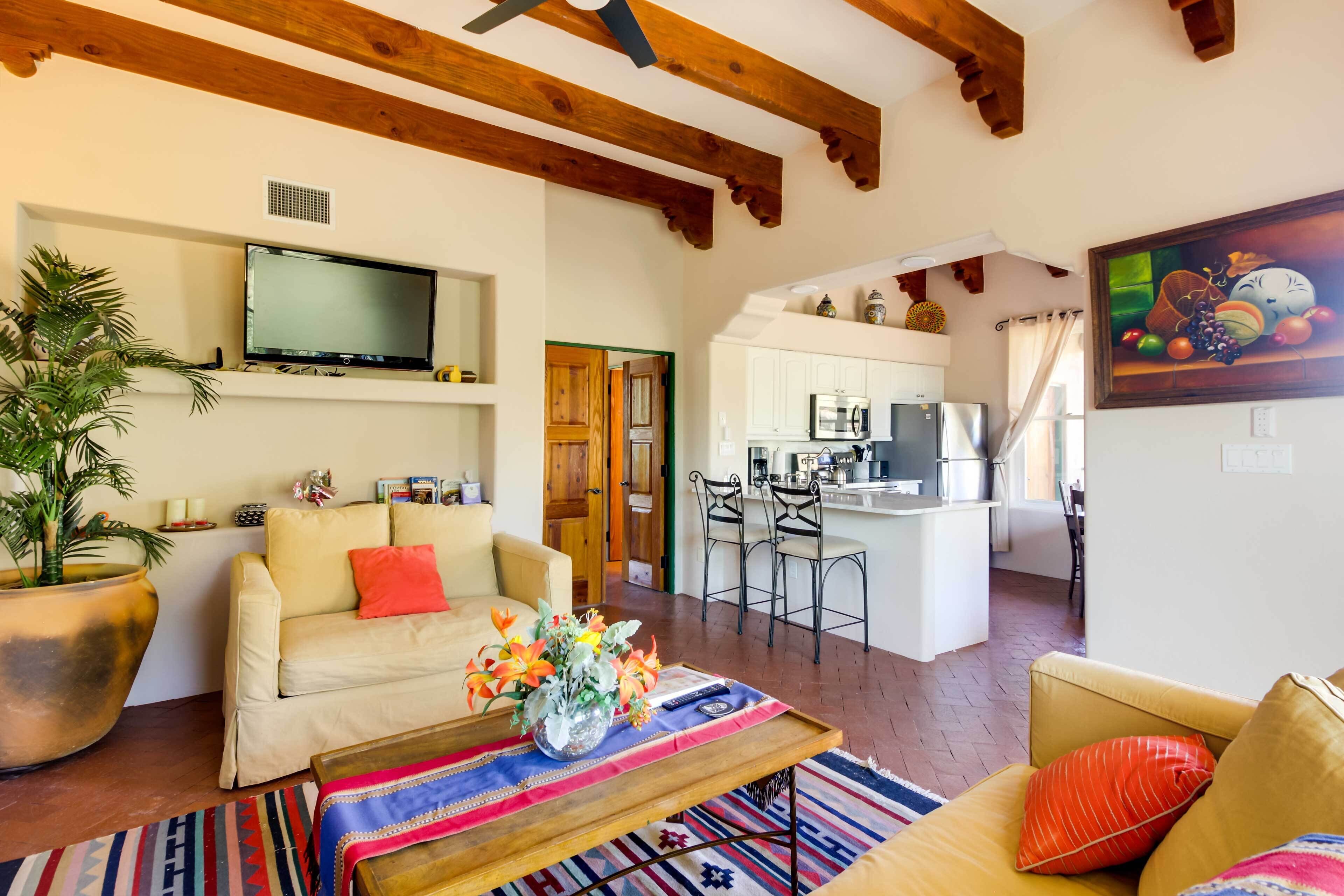 A living room with a sofa, coffee table, and TV. There's a kitchen in the background with a dining area.