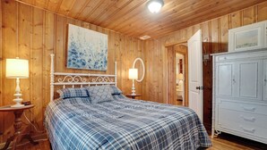 Un dormitorio con paneles de madera, una cama, dos mesitas de noche con lámparas, un aparador y un cuadro en la pared.