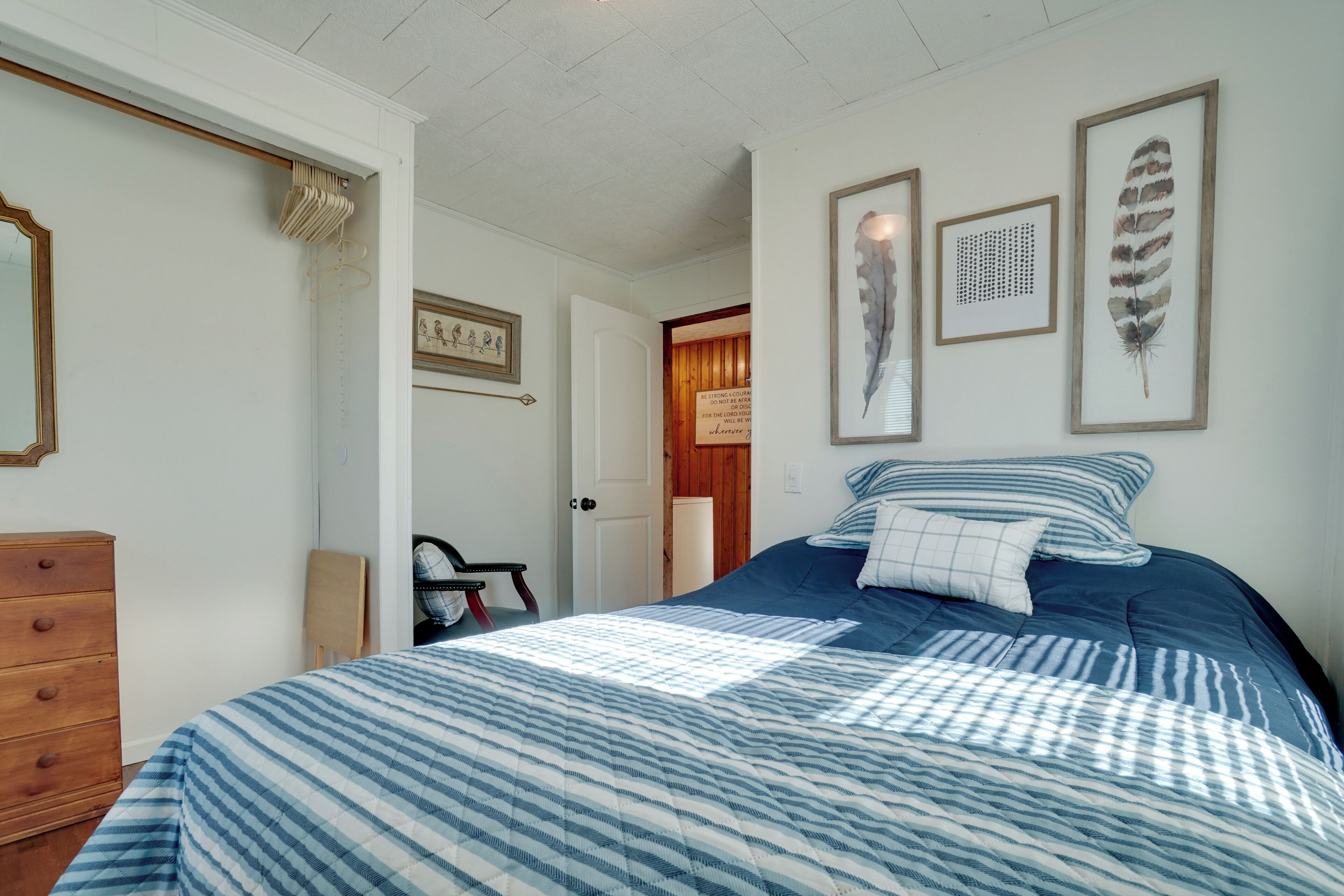 A bedroom with a bed, dresser, and framed artwork on the wall.
