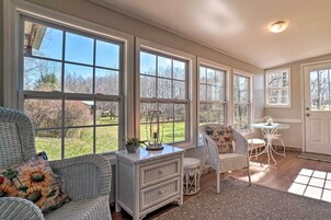 Una habitación iluminada por el sol con ventanas amplias, muebles de mimbre, una mesita y una puerta blanca.