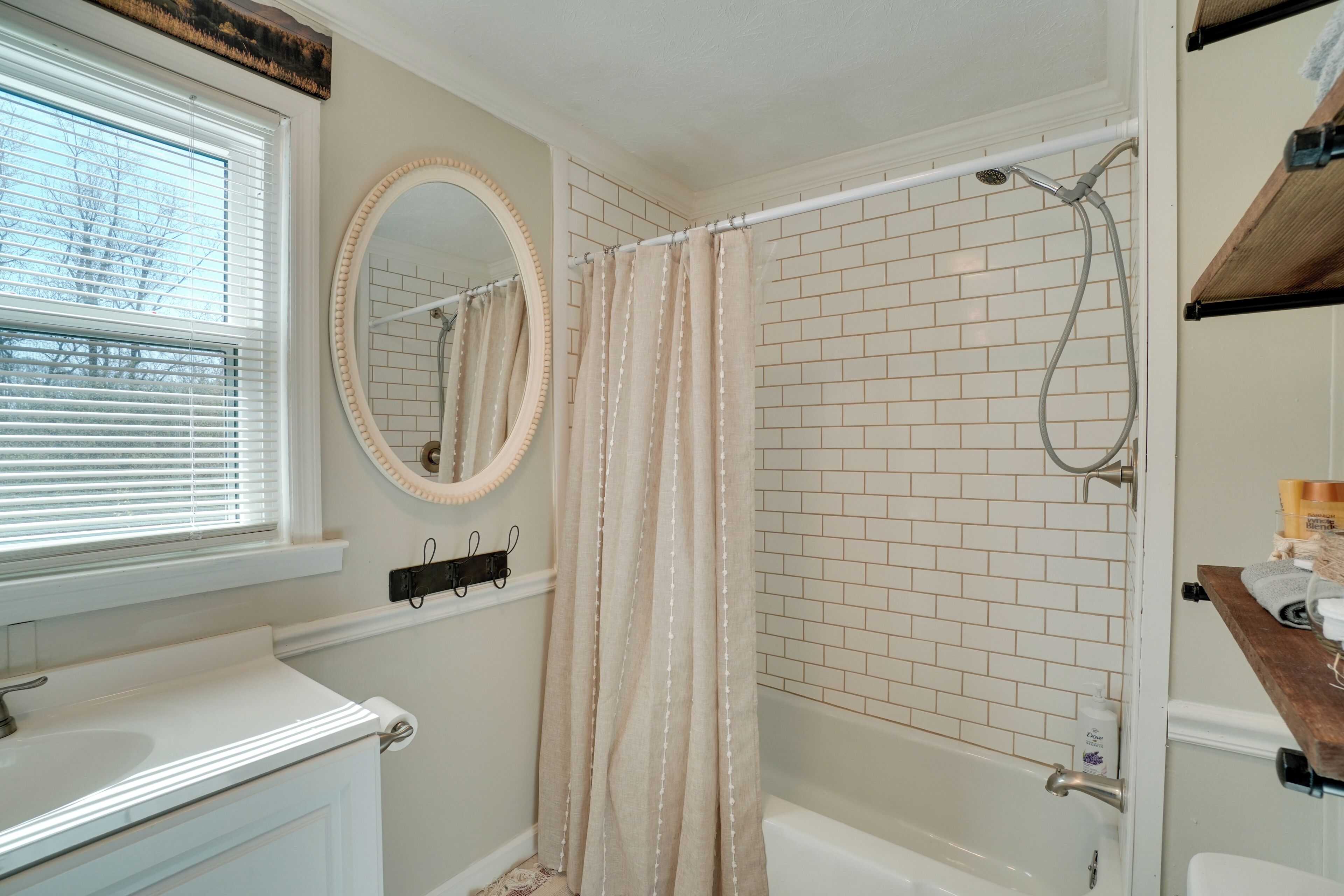 A bathroom with a white bathtub, a shower with a beige curtain, a white sink, and a mirror with a wooden frame.