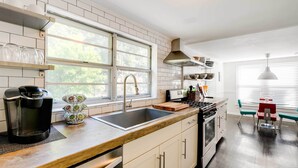 A modern kitchen with a large window, stainless steel appliances, and a dining area with a red and teal table and chairs. - New Memphis Midtown Apt: 2 mi to Overton Square! (Memphis)