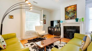 A modern living room with green sofas, a wooden coffee table, a white chair, a fireplace, and a TV. - New Memphis Midtown Apt: 2 mi to Overton Square! (Memphis)