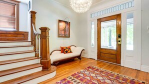 A staircase with wooden railings, a white sofa with a colorful cushion, a patterned rug, and a chandelier. - New Memphis Midtown Apt: 2 mi to Overton Square! (Memphis)