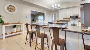 A modern kitchen with white cabinets, a central island with bar stools, a microwave, and a refrigerator. - Southern Escape in Guyton: Private Yard & Hot Tub! (Guyton)