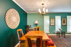 Een eetruimte met een houten tafel en stoelen, een kroonluchter en lijstwerken aan teal-kleurige muren.