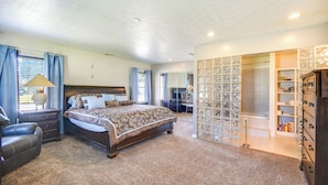 Ein Schlafzimmer mit einem großen Bett, einem Nachttisch, einem Sessel, einer Kommode und einem Ankleidezimmer mit Regalen.