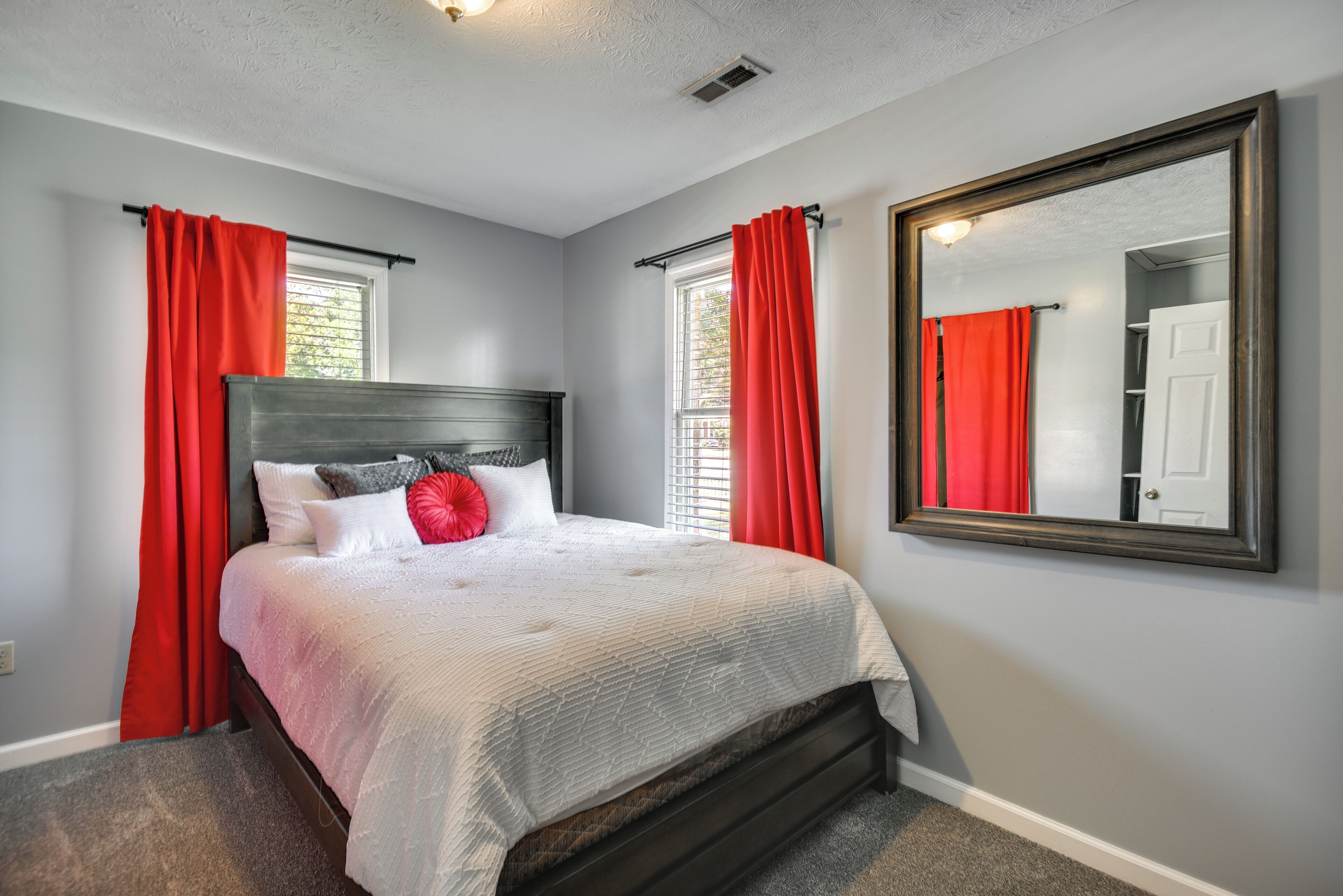 A bedroom with a bed, red curtains, a large mirror, and a window.