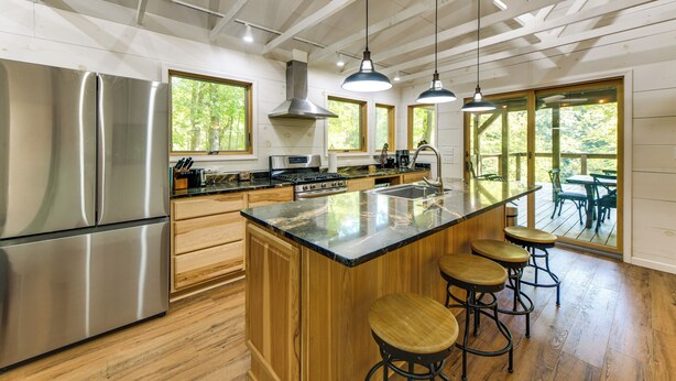 A modern kitchen with stainless steel appliances, wooden cabinetry, and a large island with bar stools. - Stunning Culloden Cabin With Deck & Creek View! (Roberta)