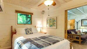 A bedroom with a wooden bed, a window with a view of trees, a ceiling fan, and a painting on the wall. - Stunning Culloden Cabin With Deck & Creek View! (Roberta)