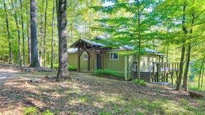 A rustic cabin with a wooden deck and a small porch, surrounded by dense forest. - Stunning Culloden Cabin With Deck & Creek View! (Roberta)