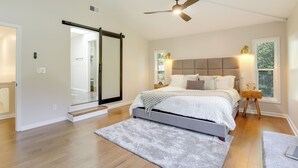 Un dormitorio con cama, ventilador de techo, ventana con vistas y puerta corrediza que da a otra habitación.