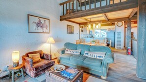 A cozy living room with a blue sofa, a brown armchair, and a wicker coffee table. A lamp and a framed picture adorn the wall. - 1 Mi to Stagecoach Lift! Homey Tahoe Townhome (Stateline)