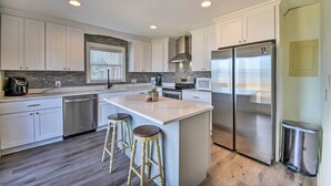 A modern kitchen with white cabinets, a stainless steel refrigerator, and a central island with stools. - Portsmouth Waterfront Vacation Rental w/ Deck (Portsmouth)