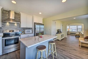 A modern kitchen with stainless steel appliances, a marble island, and wooden stools.