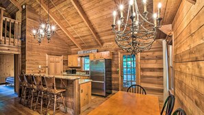 L’intérieur d’un chalet rustique en bois comprend un coin repas, des tabourets de bar, un lustre et une enseigne sur laquelle on peut lire « BIG CANOE ».
