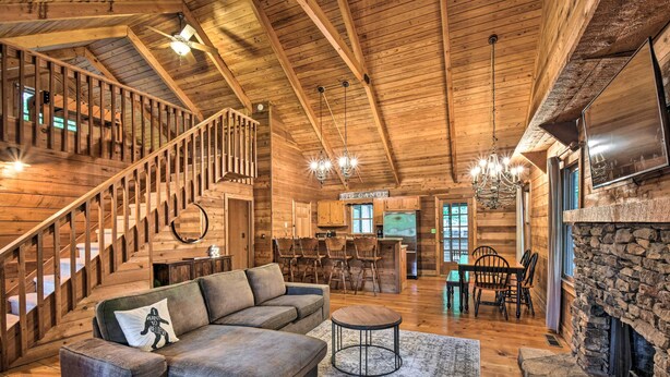 Un vaste espace de vie agrémenté d’un escalier en bois, d’un grand canapé d’angle, d’une cheminée en pierre et d’un coin repas avec des meubles en bois.
