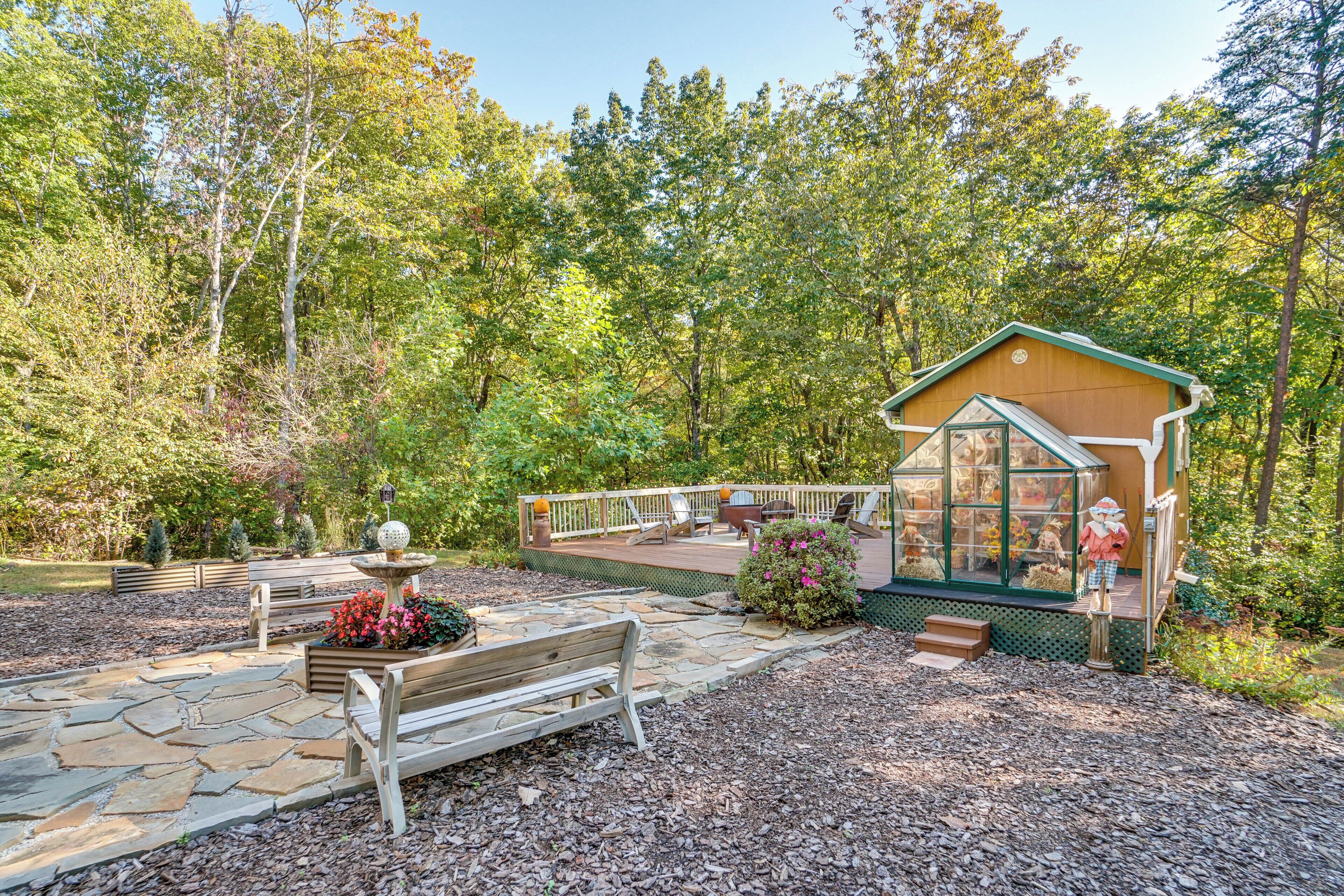 A wooden deck with a bench and a birdbath, surrounded by a stone pathway and a small garden area.