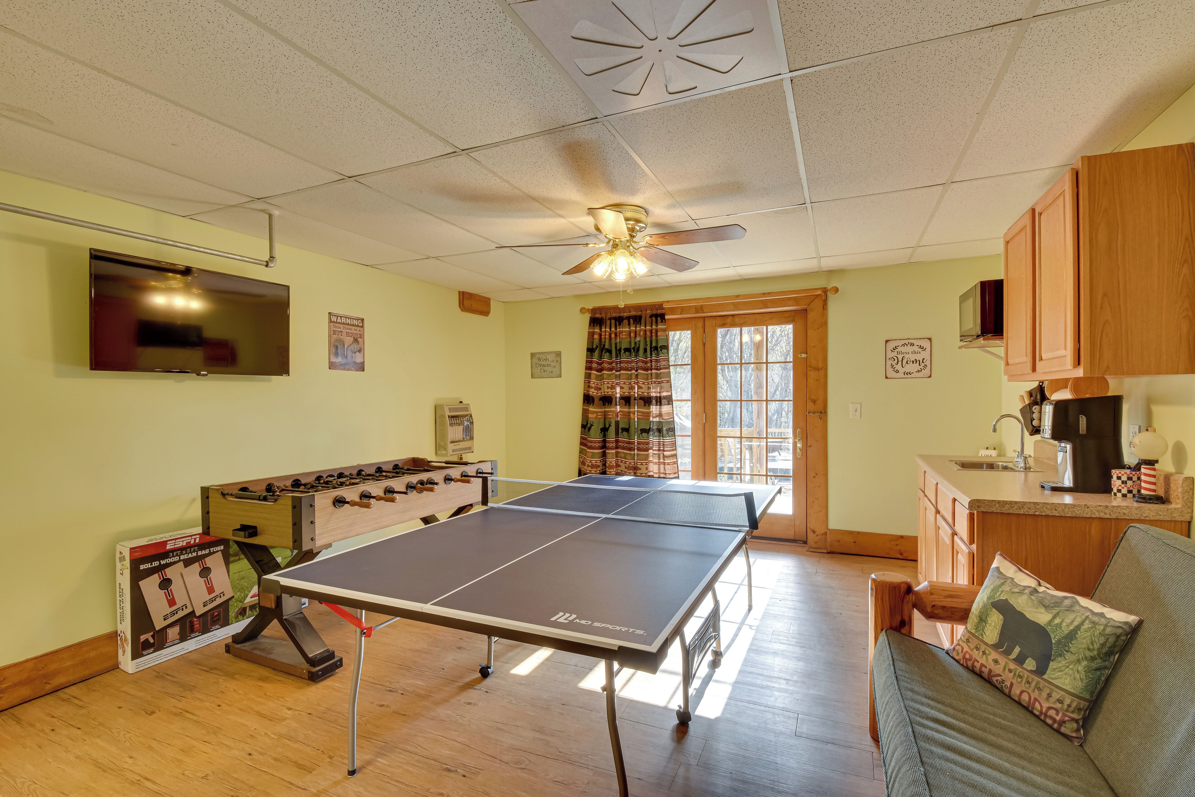 Een kamer met een tafeltennistafel, een tafelvoetbalspel, een kitchenette en een bank met een kussen.