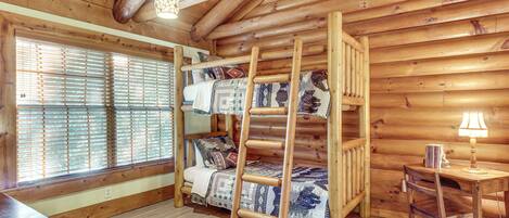 Un dormitorio tipo cabaña de madera con una litera, un escritorio y una lámpara.