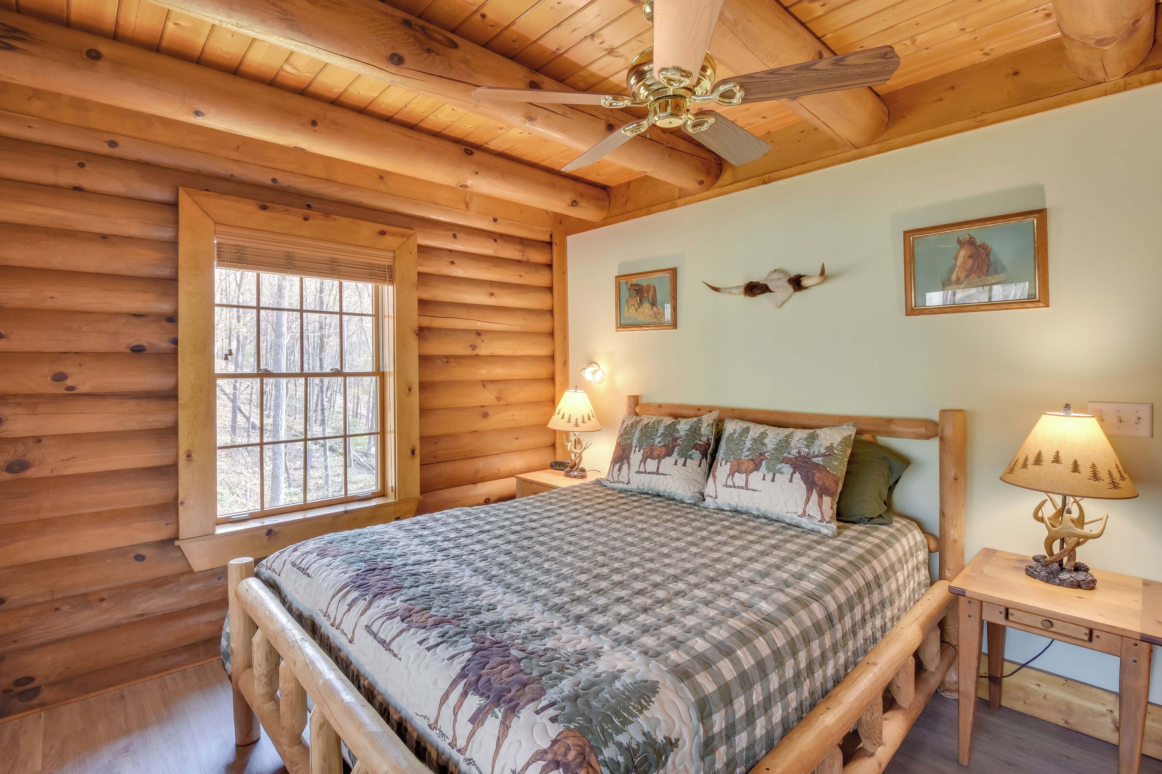 A log cabin bedroom with a bed, two wall-mounted lamps, and two framed pictures.