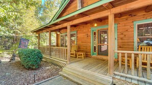 A wooden cabin with a porch, a sign indicating it is a cabin, and a small bush in front.