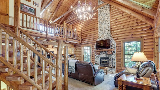 A log cabin interior with a wooden staircase, a fireplace, a leather sofa, and a television.