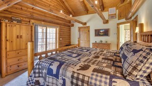 A log cabin bedroom with a large bed, wooden walls, and a ceiling fan.