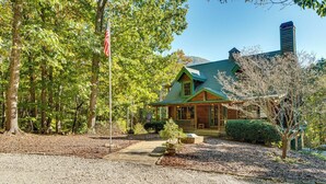 A wooden cabin with a green roof, surrounded by trees and a gravel driveway.