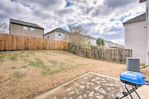 A backyard with a wooden fence, a concrete patio, and a blue grill.