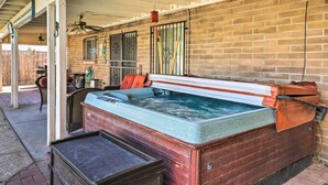 Un bain à remous doté d’une structure en bois et d’un couvercle en métal, un mur en briques et un espace patio couvert avec un ventilateur de plafond et une lanterne suspendue.