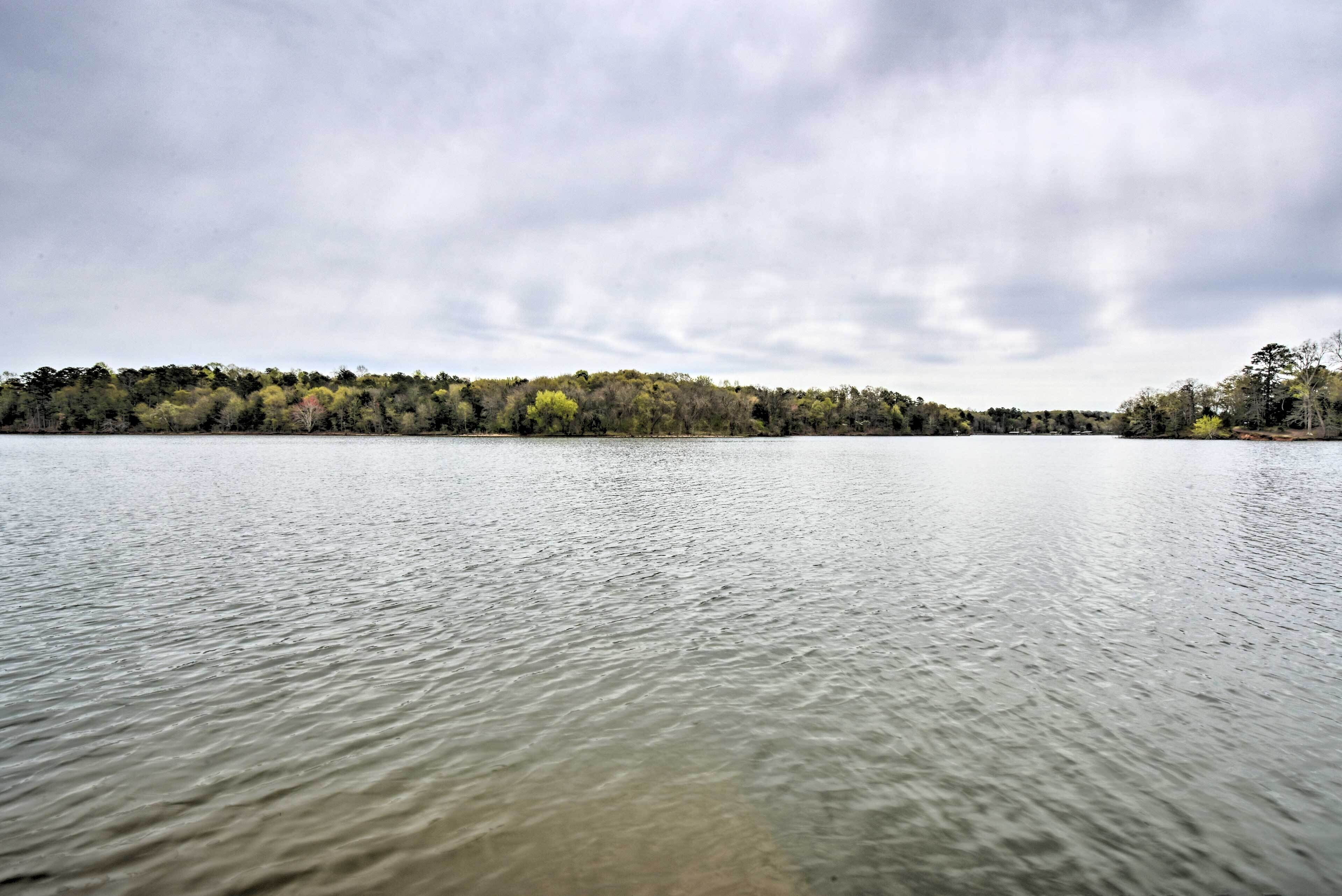 A calm lake with a forested shoreline under a cloudy sky.