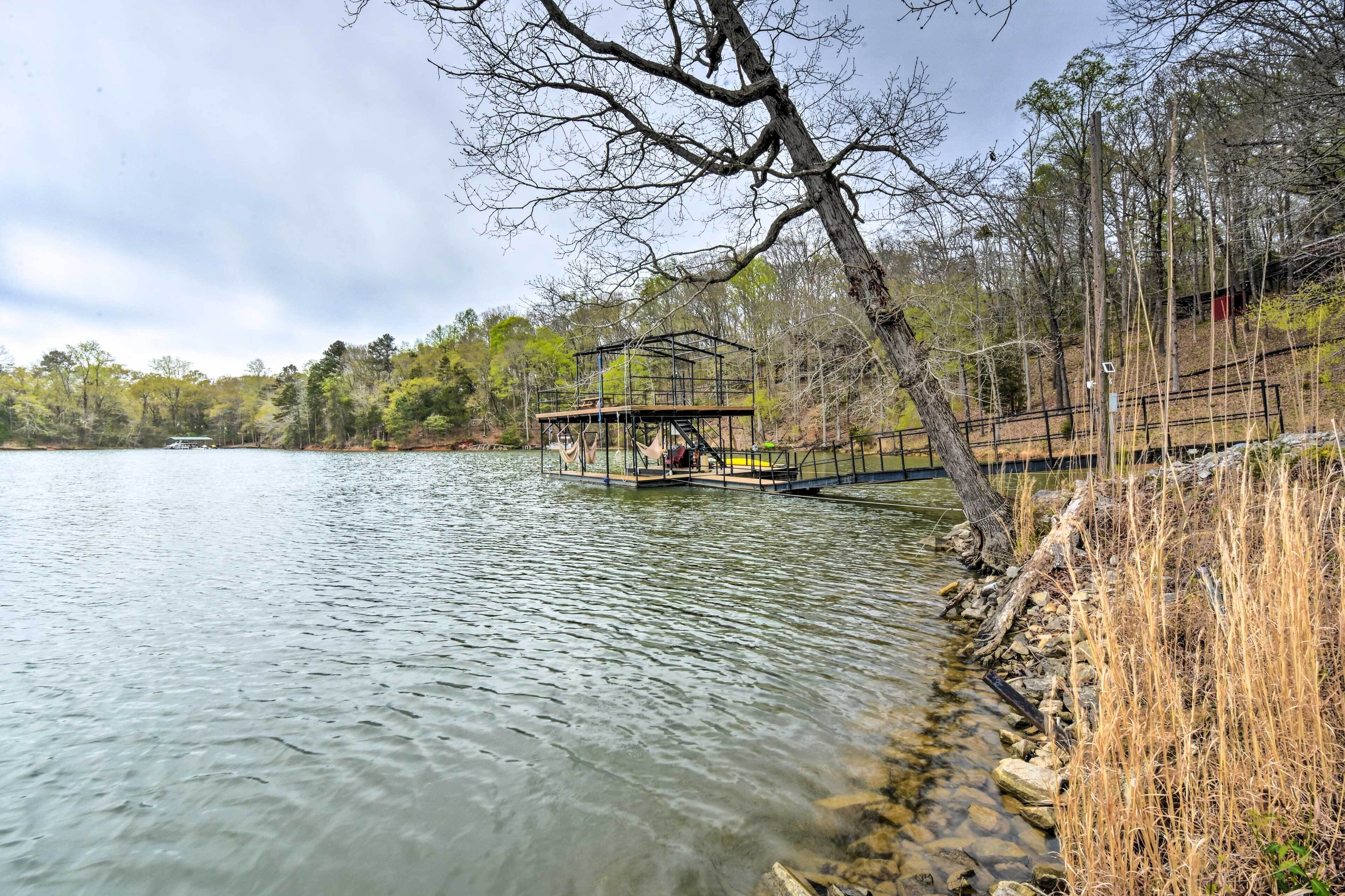 A dock extending into a calm lake with a metal structure on it, surrounded by trees and a clear sky.