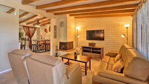Sala de estar con sofá, mesa de centro y chimenea. Hay un televisor montado en la pared y un reloj también en la pared.