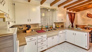 Una cocina con armarios blancos, encimera de granito y vigas de madera en el techo.