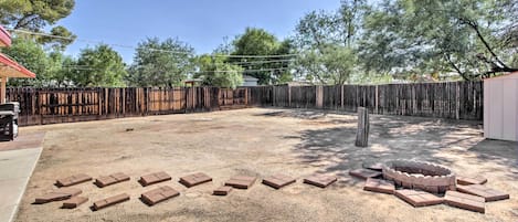 A backyard with a wooden fence, a brick fire pit, and scattered bricks.