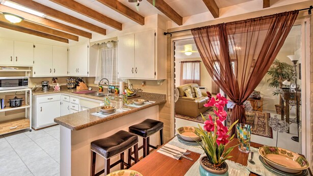Una cocina con armarios blancos, techo de madera y comedor con mesa y sillas.