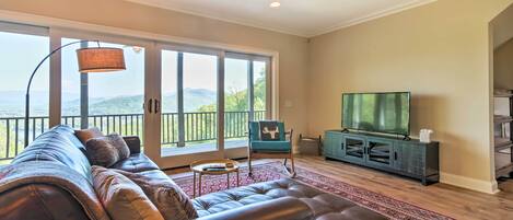 A living room with a leather sofa, a television, and a view of mountains through large windows.