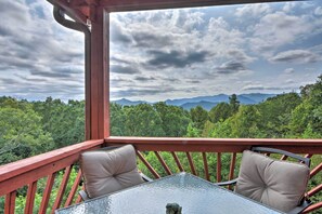 Ein Balkon mit Glastisch und zwei gepolsterten Stühlen, mit Blick auf ein bewaldetes Gebirge.