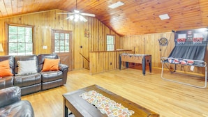 A cozy room with a wooden ceiling, a leather sofa, a foosball table, and a dartboard. - Wooded Blue Ridge Cabin: 2 Decks, Fire Pit! (Cherry Log)