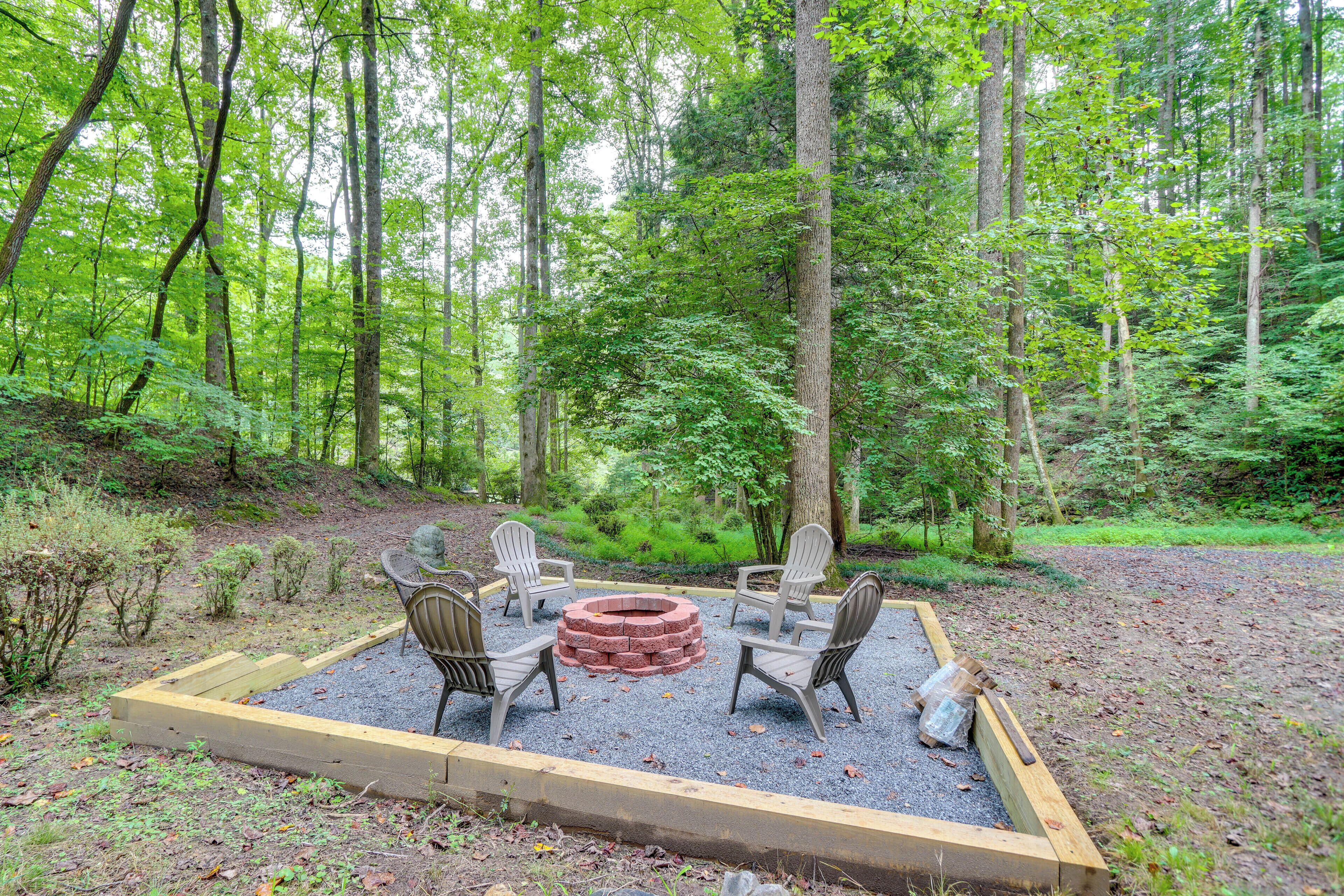A circular fire pit surrounded by four Adirondack chairs in a forest setting.