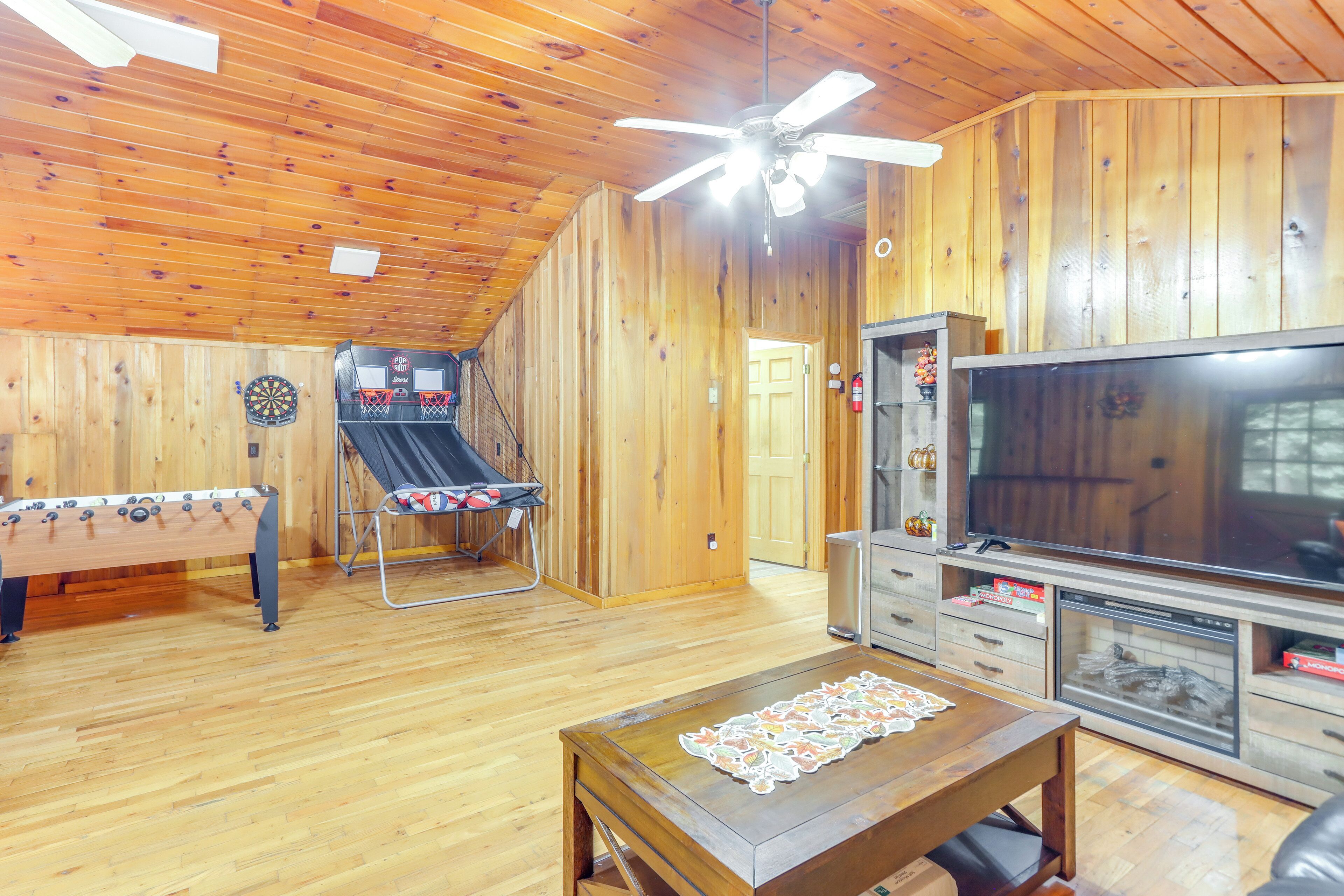 Ein Zimmer mit Holzboden, einer Kicker-Tischfußballanlage, einer Dartscheibe und einem Fernseher.